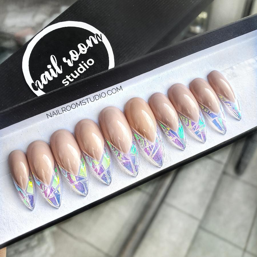 Long nude stiletto nails with a modern broken glass effect, featuring gold, green, and blue iridescent accents by Nail Room Studio