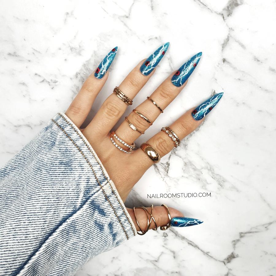 Shiny blue long nails by Nail Room Studio in stiletto sculpted style with glitter, lightning design, glitter and rose accents for a striking look