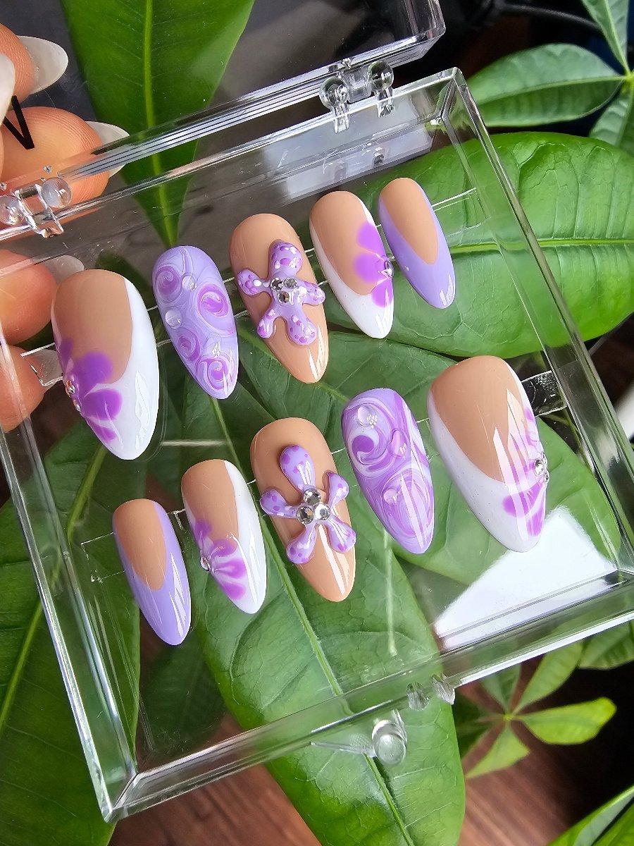 Nails in clear box, nails in almond shape with white deep french hand painted style and lilac water painting accents with small crystals