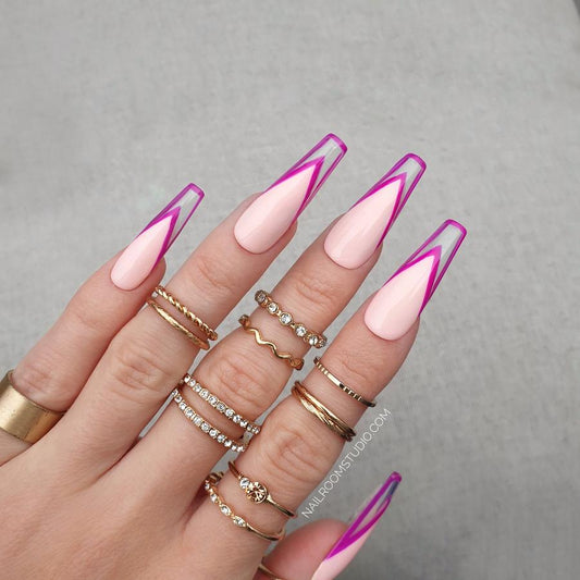 Long coffin nails in a soft honey pink base with an intense purple French outline, showcased on a hand adorned with gold rings