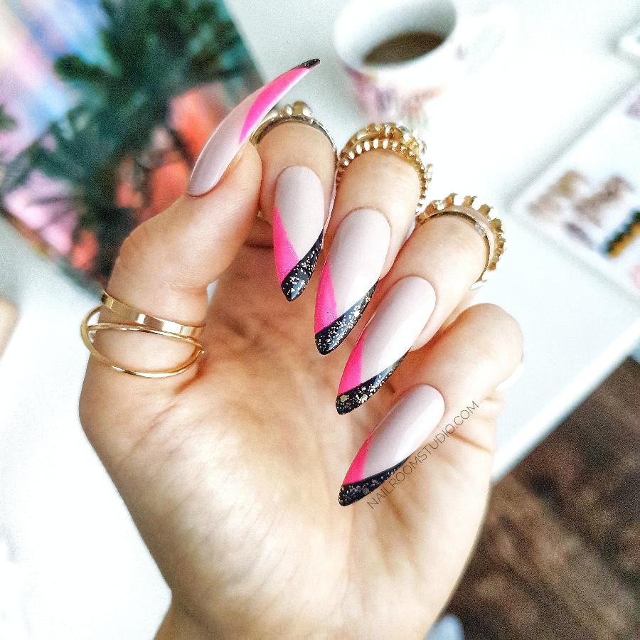Long French nails with beige base and bold geometric pink and black tips, highlighted with a touch of sparkle
