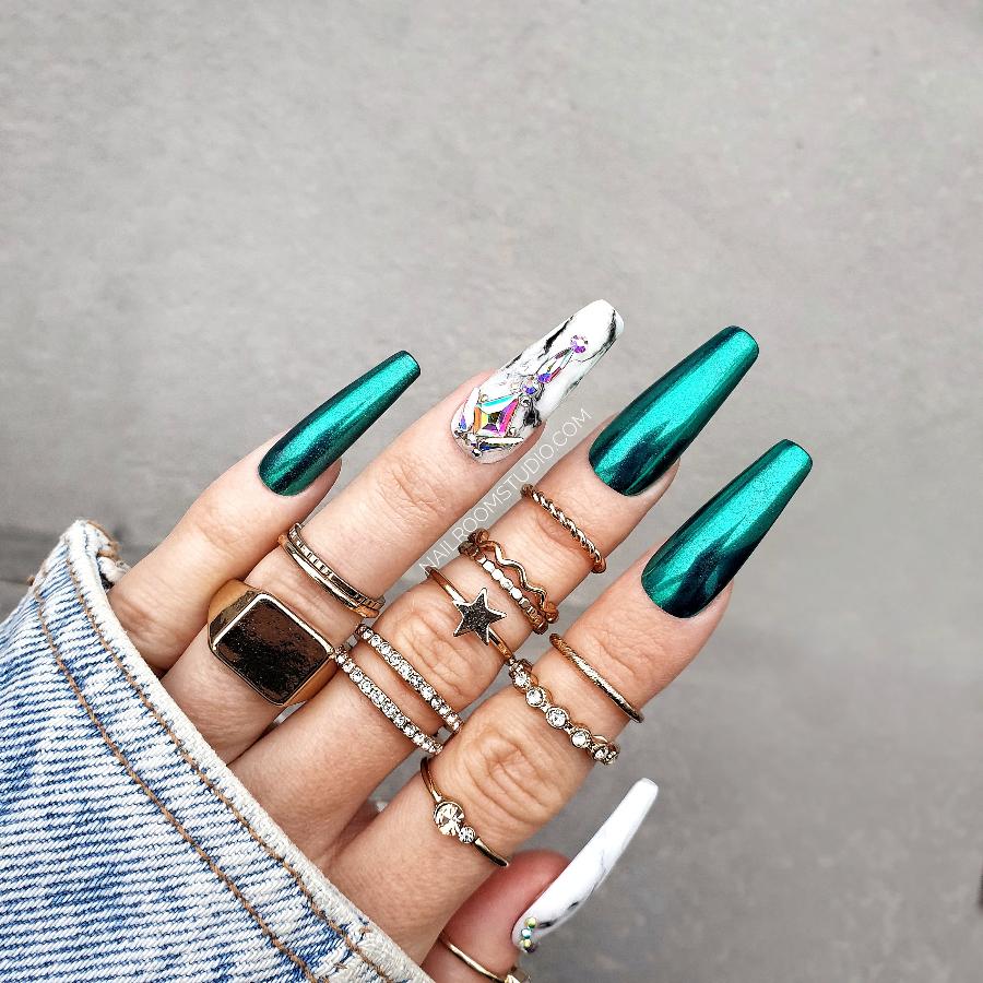 Green chrome nails with black and white marble accent nails and Swarovski crystal embellishments, showcased on a hand with long, glossy nails