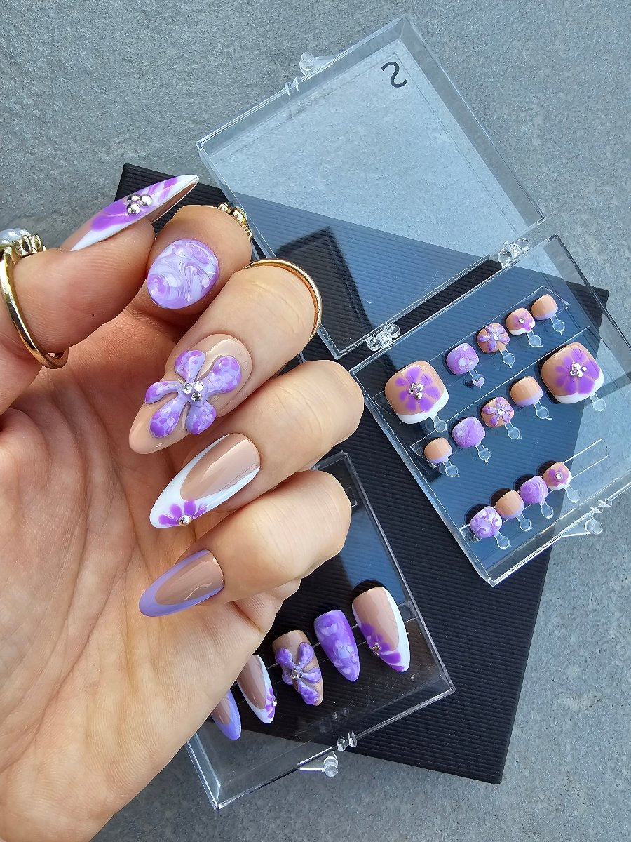 White woman hand wearing cistom press on nails in nude color, waterpainting, flowers and deep french, in the back two boxes with matching toes pop on nails