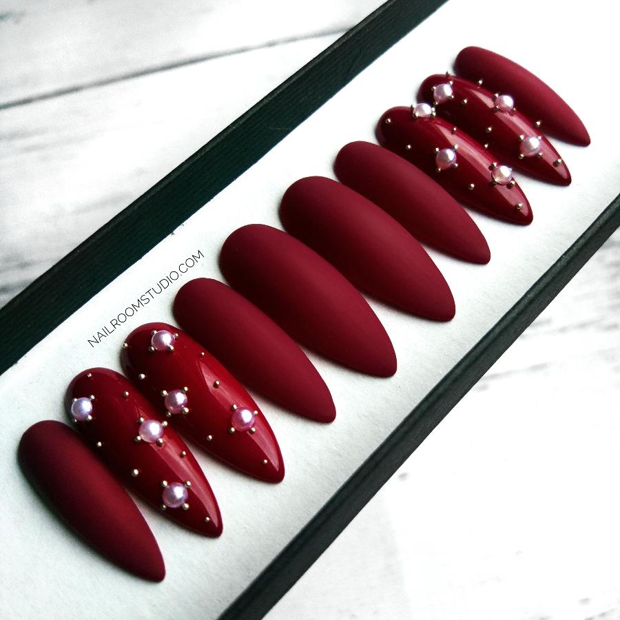 Burgundy long stiletto nails with a mix of matte and glossy finishes, detailed with pearls and crystals by Nail Room Studio