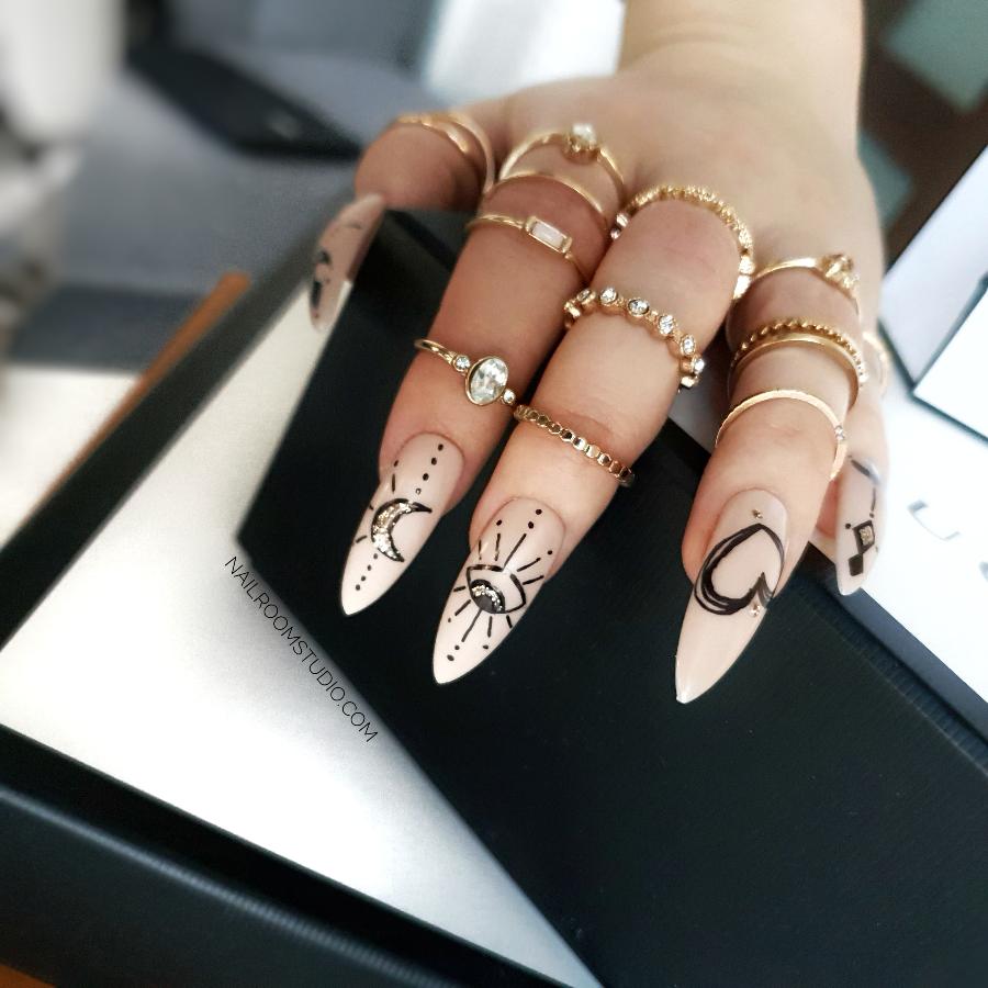 Long stiletto witchy nails adorned with artistic drawings of mystical symbols, including suns and moons on a nude background by Nail Room Studio