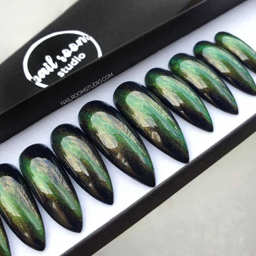 Stylish stiletto nails in dark green with cat-eye shimmer and a witchy vibe, designed by Nail Room Studio