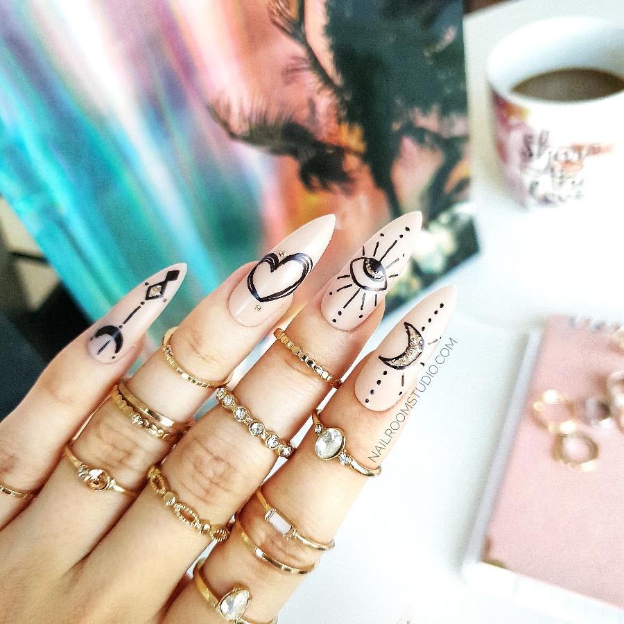 Elegant witchy stiletto nails featuring artistic designs of moons and hearts, perfect for a mystical look by Nail Room Studio