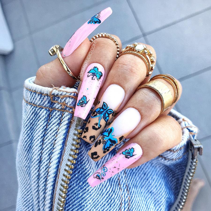 Full set of girly press-on nails for summer, showcasing vibrant light pink with panther spots, blue butterflies, and floral accents by Nail Room Studio