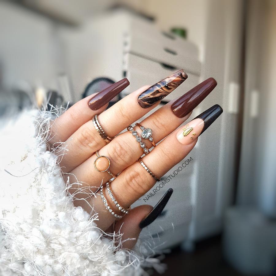 Elegant fall nails with a beige marble design, glossy finish, small gold feather detail, and french tip on one nail, available for both manicure and pedicure by Nail Room Studio