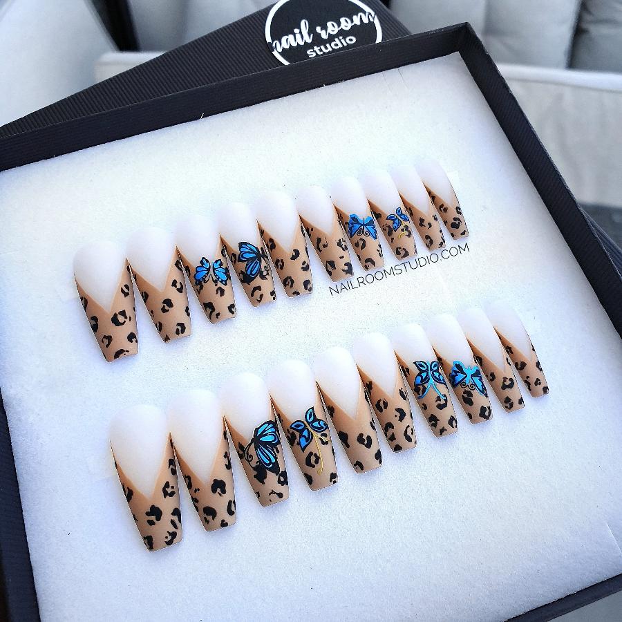 Long sculpted coffin nails in a full set of 20 featuring handmade panther print on french tips with blue butterfly motifs and stylish brown and beige tapes by Nail Room Studio