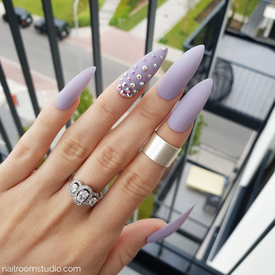 Matte lilac stiletto nails featuring Swarovski crystal accents for a refined look by Nail Room Studio