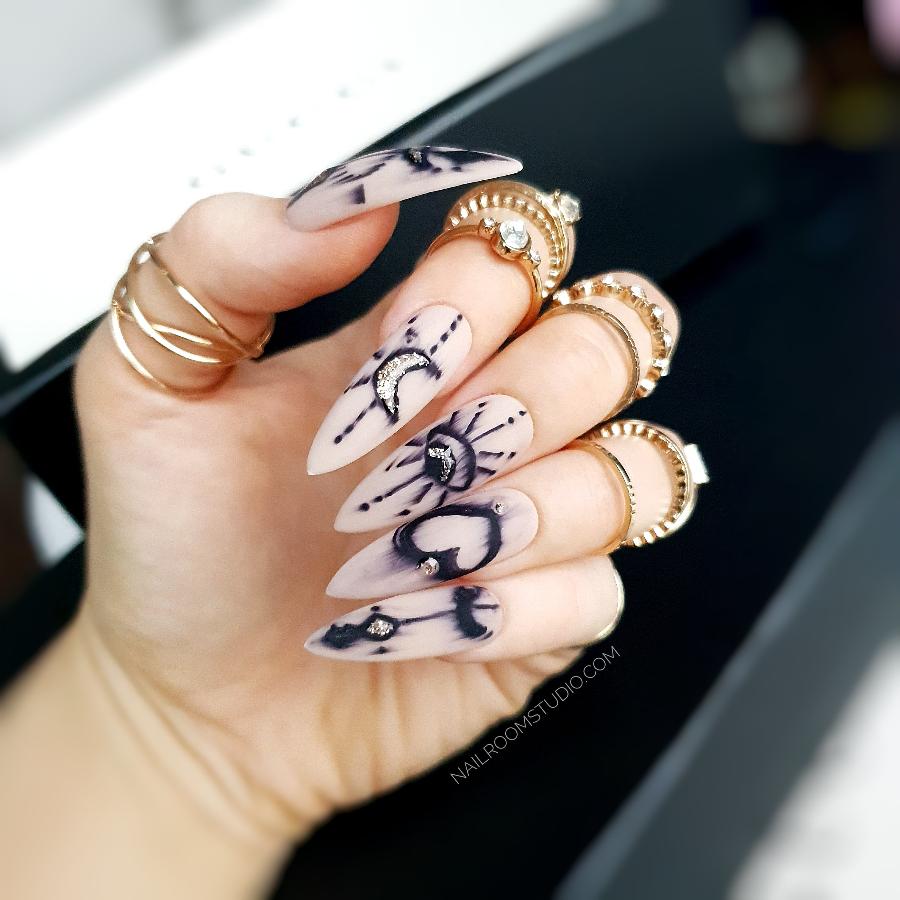 Long stiletto press-on nails in nude tones with intricate witchy ink hand painted symbols like arrows, hearts, and moons by Nail Room Studio