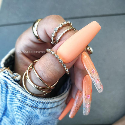 Juicy orange long coffin nails with glossy and matte finish, chrome glitter accents, and ombre with milky transparent tips, vibrant for summer, available with matching toe nails by Nail Room Studio