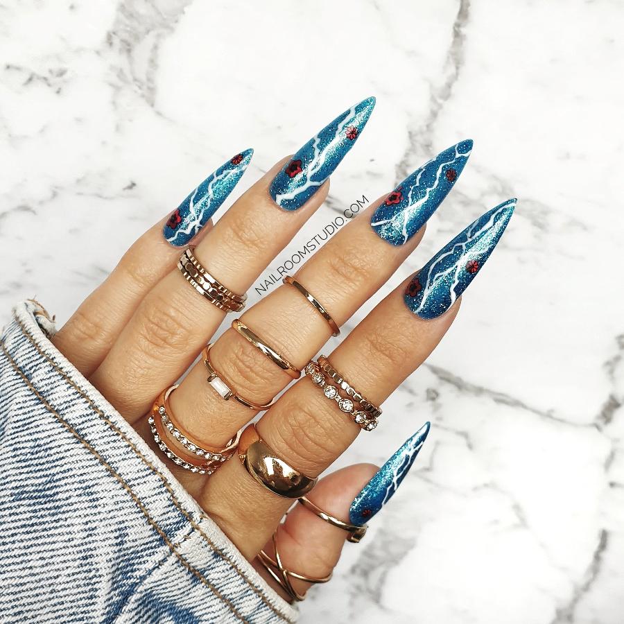 Glossy blue nails by Nail Room Studio in long sculpted style with glitter, red rose design, and lightning accents for a bold statement