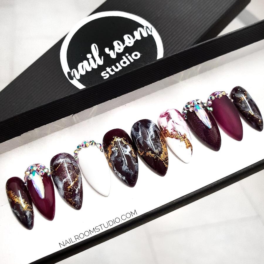 Long burgundy coffin nails with black and white marble details and gold crystal accents by Nail Room Studio