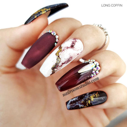 Burgundy matte coffin nails with black and white marble patterns and gold crystal details by Nail Room Studio