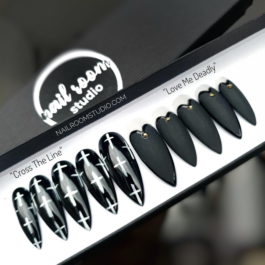 Long black stiletto faux nails featuring witchy crosses, matte and glossy finishes, with gold crystals and transparent heart details by Nail Room Studio