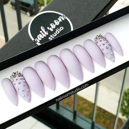 Alt text: Chic matte lilac stiletto nails adorned with Swarovski crystals, designed by Nail Room Studio shop