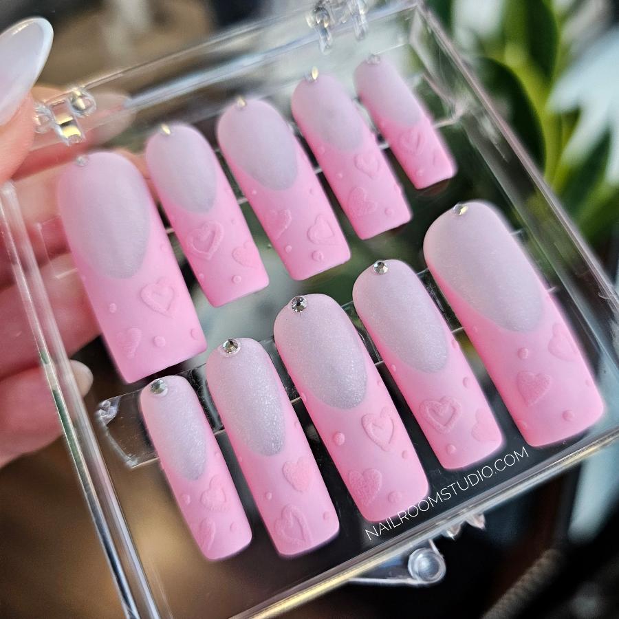 Chic powder pink matte press-on nails with delicate crystal details, long square design, perfect for romantic occasions like Valentine's Day or gender reveal parties, featuring charming heart patterns