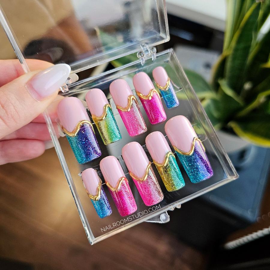 Vibrant long pink press-on nails with jelly-like transparency and rainbow tips in various colors, adorned with unique golden 3D designs, ideal for making a bold statement, for LGBTQ plus community