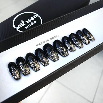 Shiny black coffin nails presented in a sleek black box, with gold glitter ombre tips for a glamorous finish