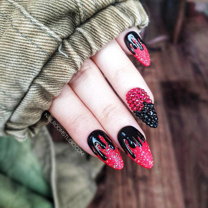 Matte red and black Halloween-inspired nails with glossy black drip design, capturing a witchy, ghostly vibe with one Swarovski crystal-accented nail, shown on hands for a dramatic effect