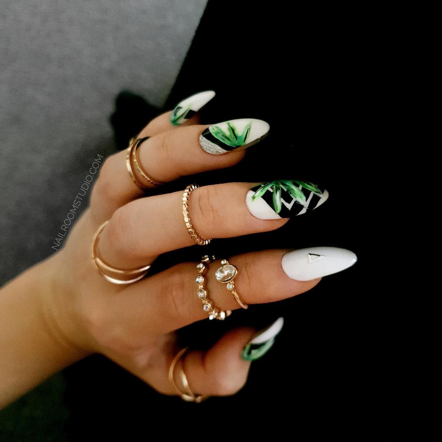 Nails in a white base with intricate black geometric shapes and green jungle accents, styled with rings on hands for a modern touch