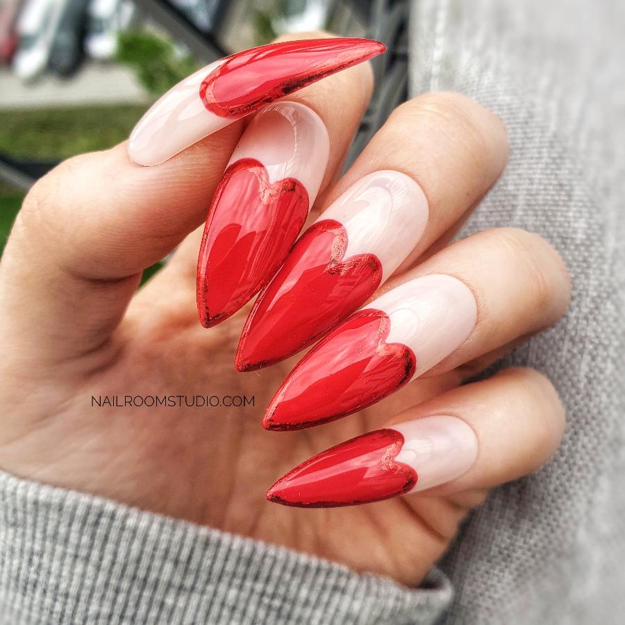 Charming pink press-on nails with red heart-shaped French tips, each outlined in chrome, for a cute and romantic look, great for dates, displayed on hands