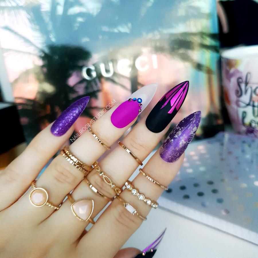 Dark matte purple stiletto nails with black accents and raindrop details, enhanced with crystals for a unique, magical appearance