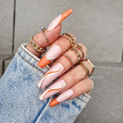 Chic powder pink nails with orange French tips and artistic gold and orange wave accents, presented as long Press-On nails on a hand