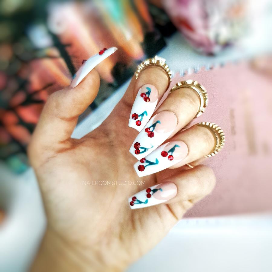 Classic French nails featuring hand-painted cherries with red Swarovski crystals adding a playful touch to the elegant design