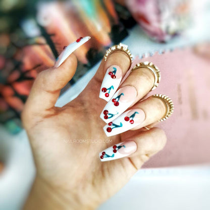 Classic French nails featuring hand-painted cherries with red Swarovski crystals adding a playful touch to the elegant design