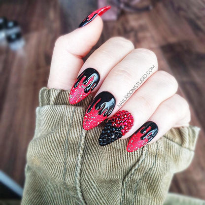 Gothic-themed Halloween press-on nails in deep red with black dripping design, featuring one glossy accent nail with dark Swarovski crystals, creating a bold witchy look on hands