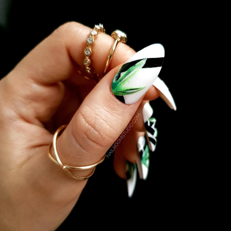 Elegant nails with black geometric elements and lush green botanical accents, shown on hands adorned with rings to highlight a jungle-inspired theme