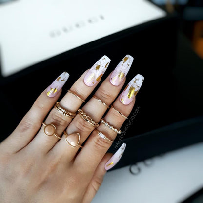 Long ballerina nails featuring a soft ombre of powder pink and white with touches of shimmering gold chrome