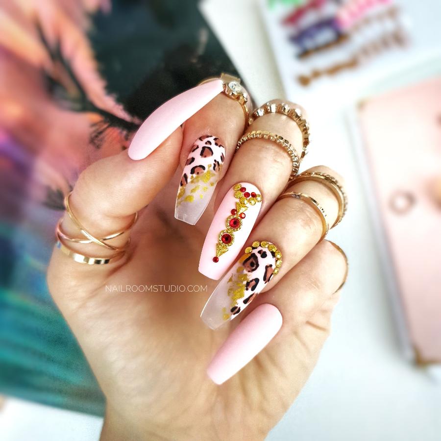 Matte nails with diagonal geometric French tips, hand-painted leopard print, and oriental accents featuring crystals and metallic elements for a unique, exotic look with sparkling red crystals