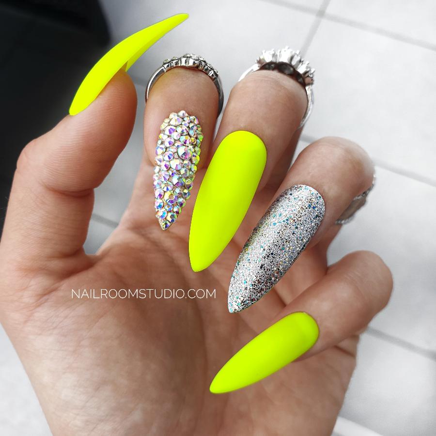 Bold matte neon yellow stiletto press-on nails with one nail decorated in silver chrome and another fully encrusted with sparkling opalescent Swarovski crystals, shown on hands, ideal for a vibrant summer look