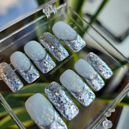 Winter-inspired Press On nails in milky, with touches of silver chrome, glitter, and french style, arranged in a box – perfect for holiday vacation styling