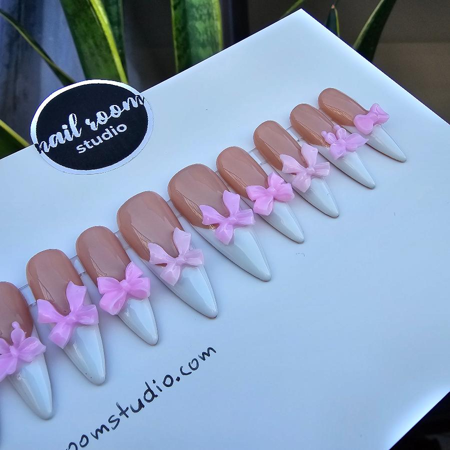 Lovely nude press on nails with white French tips and delightful pink 3D bows, designed in a sculpted stiletto style for a feminine touch