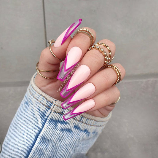 Elegant coffin nails in a delicate pink shade, with a bold purple outline in a French style, displayed on a hand with gold rings