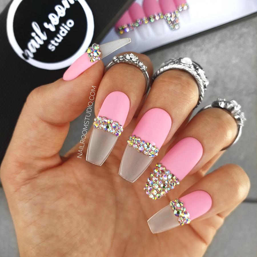 Matte pink press-on nails with transparent French tips adorned with opalescent silver Swarovski crystals, displayed on hands in ballerina coffin shape