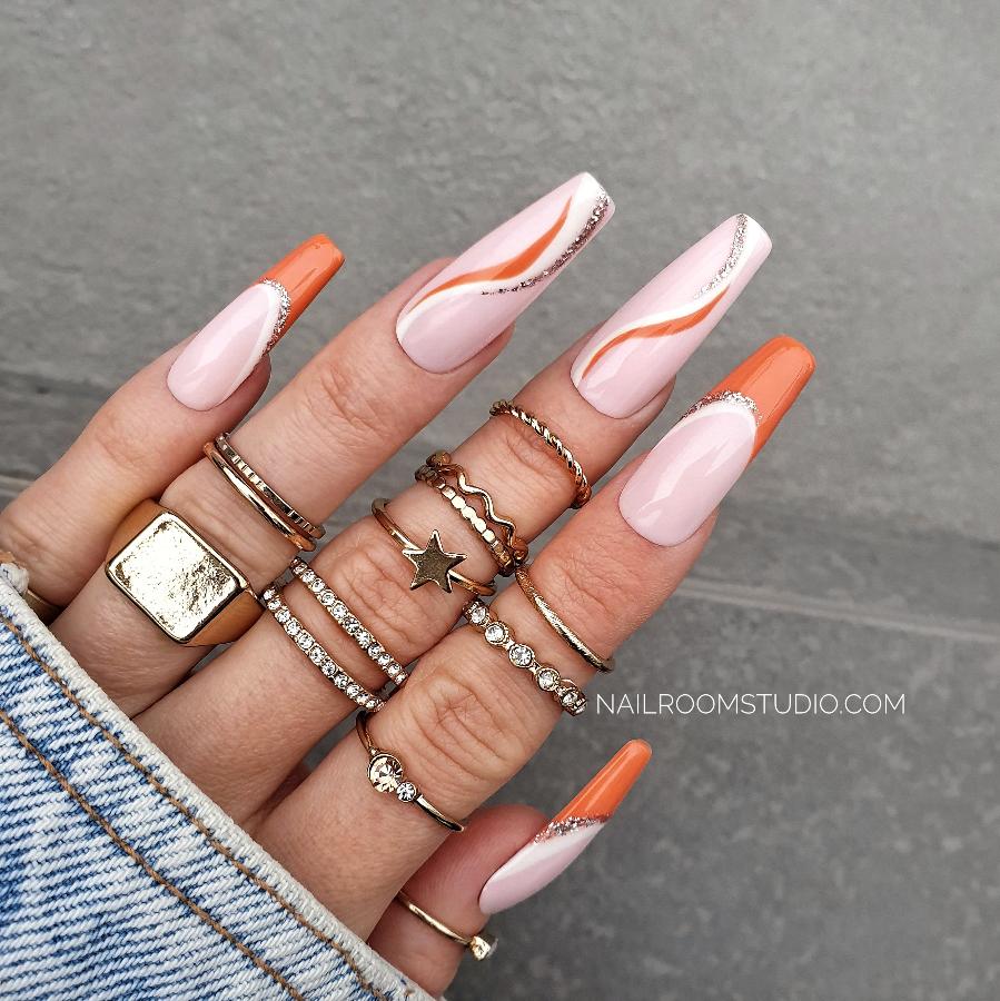 Powder pink Press-On nails featuring stylish orange French tips and hand-painted wave accents in gold and orange, beautifully displayed on a hand