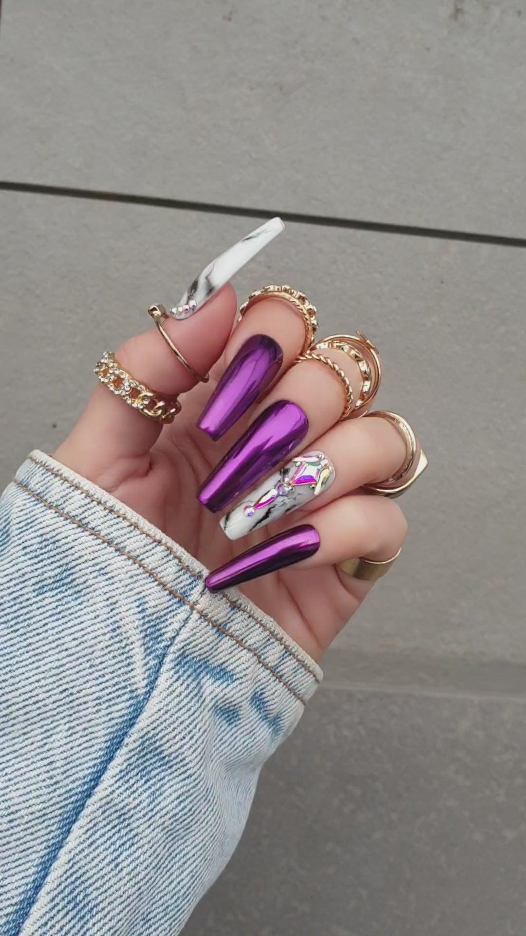 Shiny pink Press-On nails with purple chrome and marble accents in black and white, finished with opal Swarovski crystals on a hand display