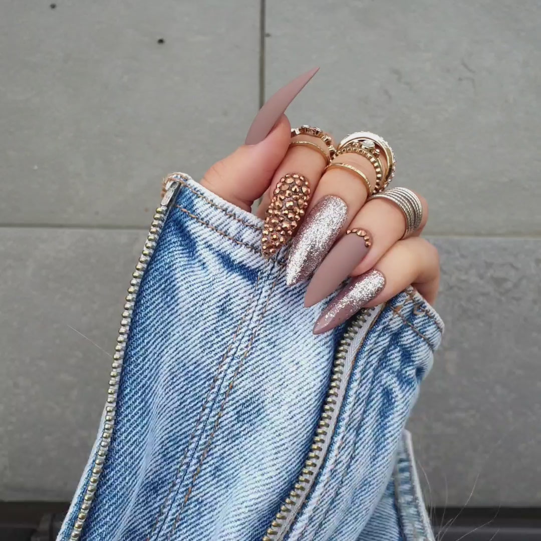 Matte light beige faux nails with cappuccino shades, featuring an accent nail filled with brown chrome Swarovski crystals from Nail Room Studio