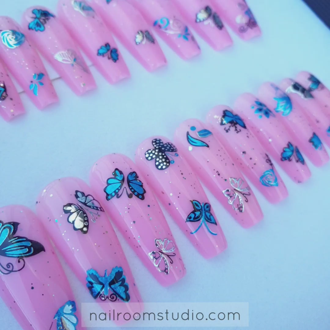 Summer-ready full set of 20 vibrant pink nails featuring long sculpted cupping and silver, glitter multicolor and blue butterfly accents, perfect for the beach by Nail Room Studio