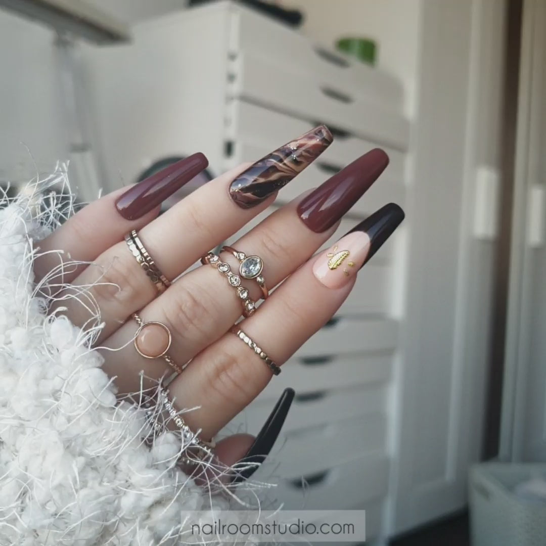 Elegant fall nails with a beige marble design, glossy finish, small gold feather detail, and French tip on one nail, available for both manicure and pedicure by Nail Room Studio