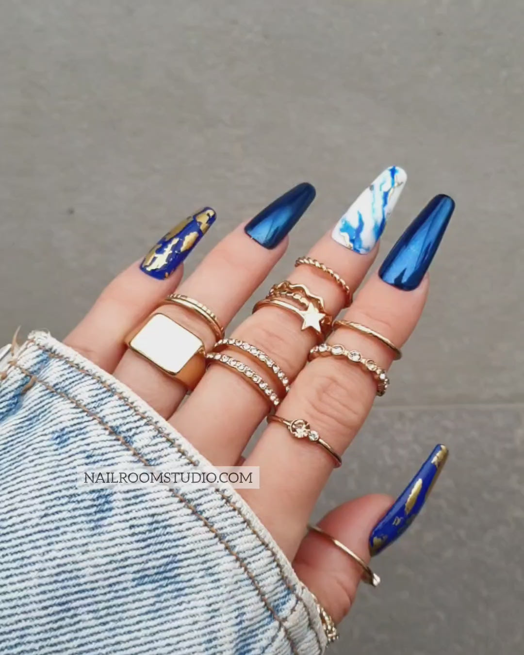 Navy blue chrome faux nails with gold chrome accents and hand-painted blue and white marble designs, available in all sizes