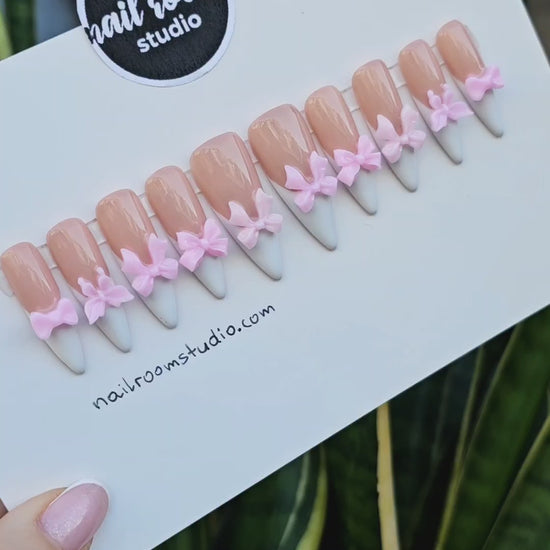 Adorable nude press on nails featuring sharp sculpted stiletto shapes and charming 3D pink bows on each nail for a playful finish