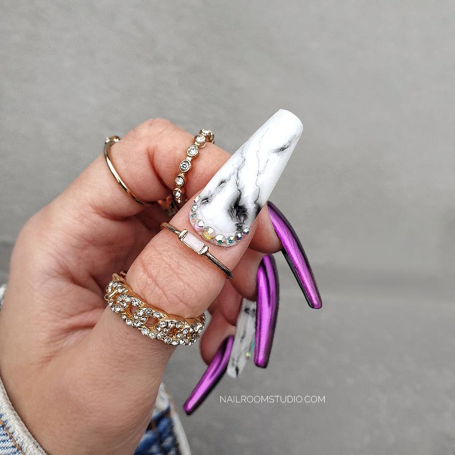 Deep purple and pink chrome Press-On nails with a black-and-white marble accent and iridescent Swarovski crystals, displayed on a hand with long coffin nails