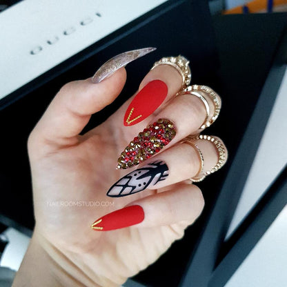 Deep red femme fatale nails with lace accents adorned with gold and red Swarovski crystals featuring a bold chrome gold finish for a seductive daring look, perfect for Christmass